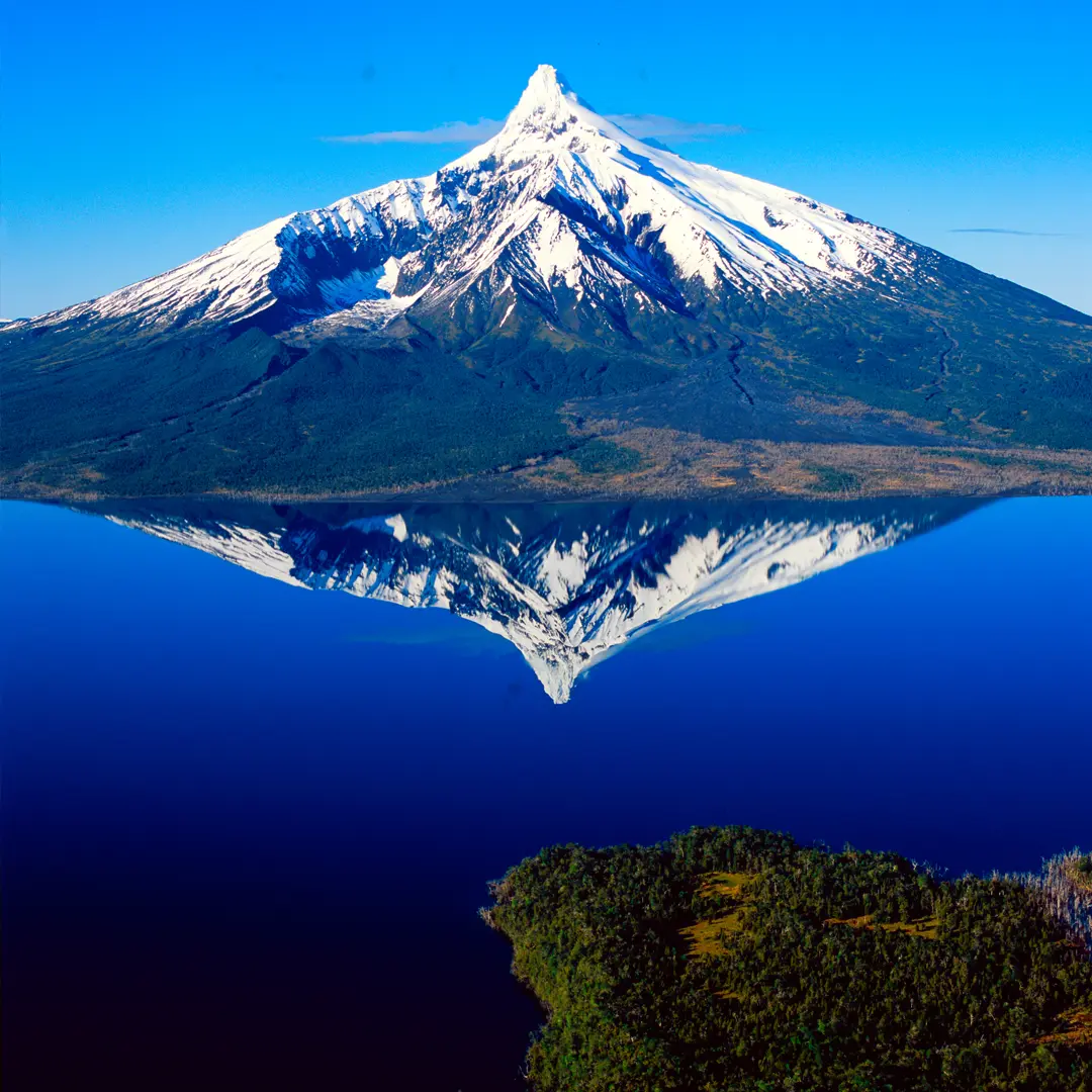 Volcán nevado reflejado en las aguas de un lago cerca del Parque Nacional Corcovado