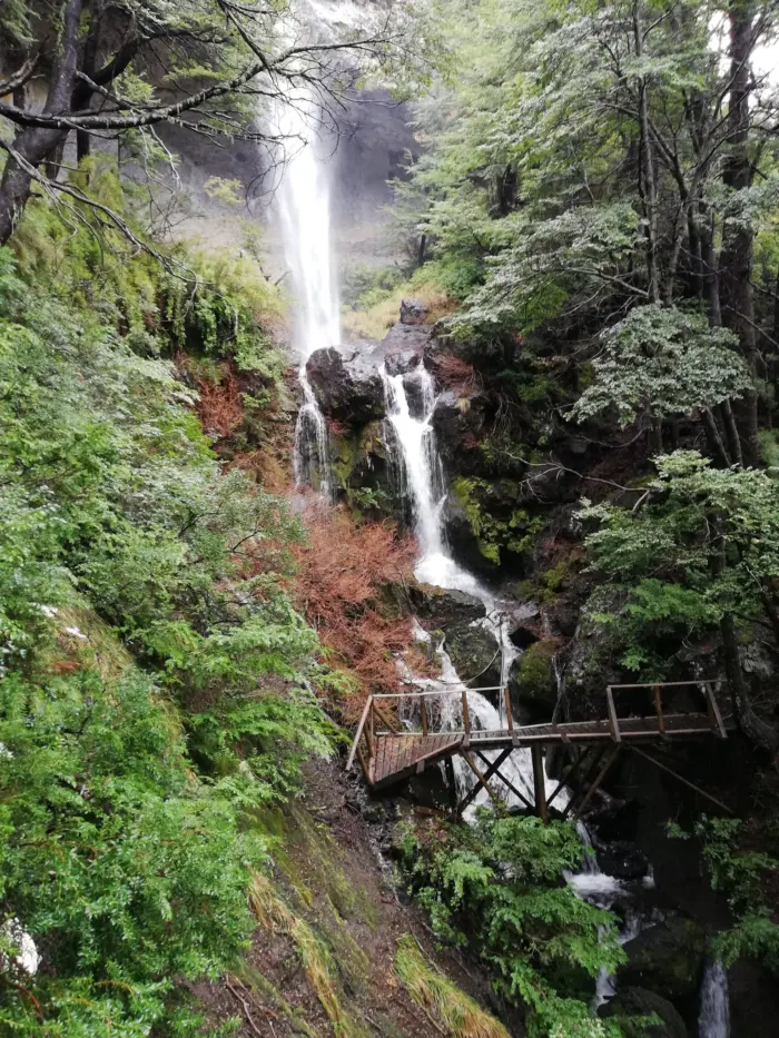 Cascada entre rocas y vegetación con un puente de madera en la Gruta del Pangue, en Ñuble