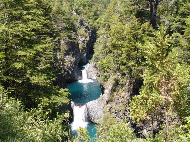 Cascada con poza azul entre bosque y roca en Radal Siete Tazas