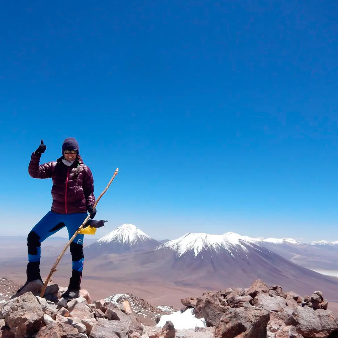 Excursionista con bastones en la cima del Cerro Toco, con volcanes nevados al fondo