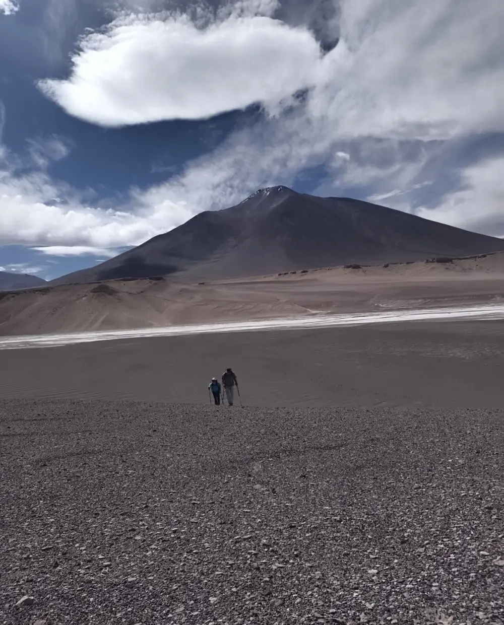 Excursionistas caminando por un llano de arena volcánica con un volcán al fondo