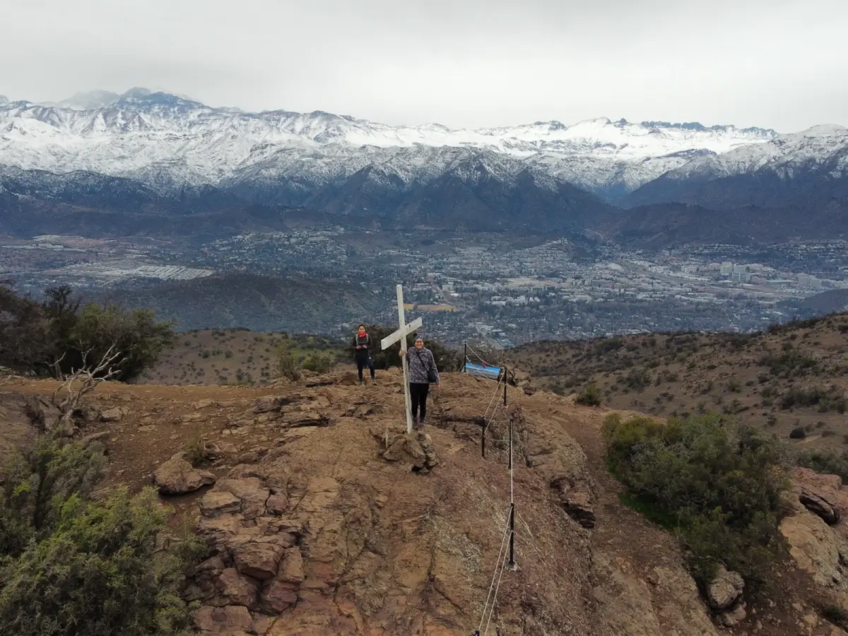 Excursionistas en un cerro con la cordillera nevada al fondo, en los alrededores de Santiago