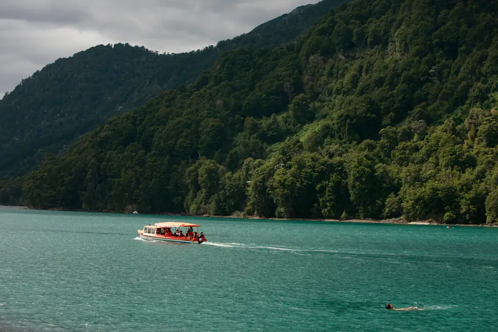 Lancha navegando por las aguas verdes del lago Todos los Santos entre montañas boscosas