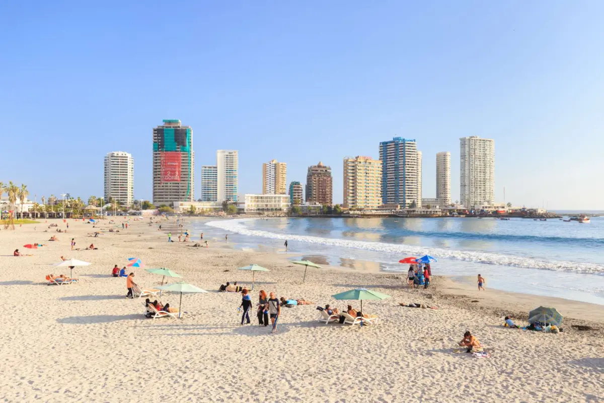 Playa de Iquique con bañistas bajo toldos y edificios de gran altura al fondo
