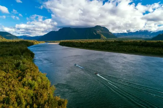 Río ancho entre montañas y bosque en la Patagonia chilena con una lancha navegando