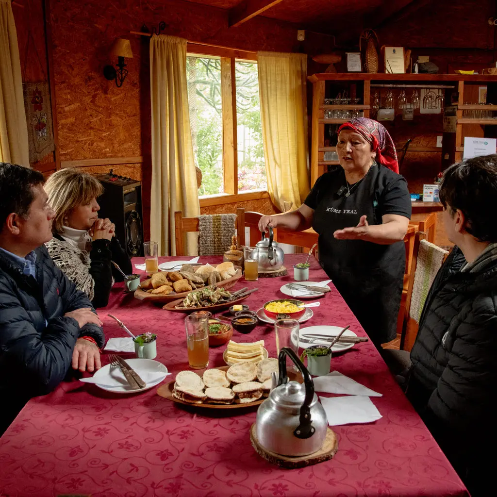 Mesa con alimentos tradicionales y anfitriona mapuche en una experiencia gastronómica en Llifén