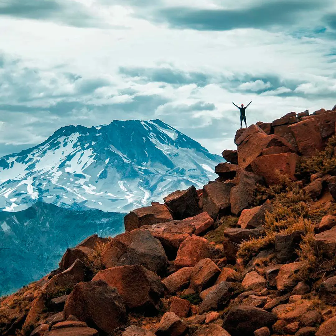 Persona en lo alto de rocas rojizas con un volcán nevado al fondo en el sendero Enladrillado
