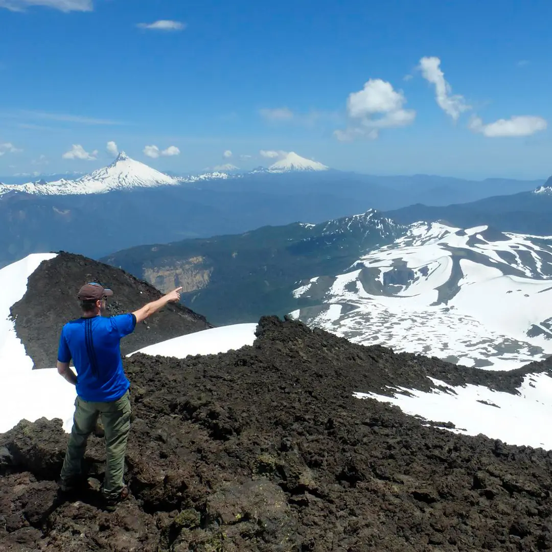 Excursionista señalando los volcanes nevados desde el volcán Casablanca