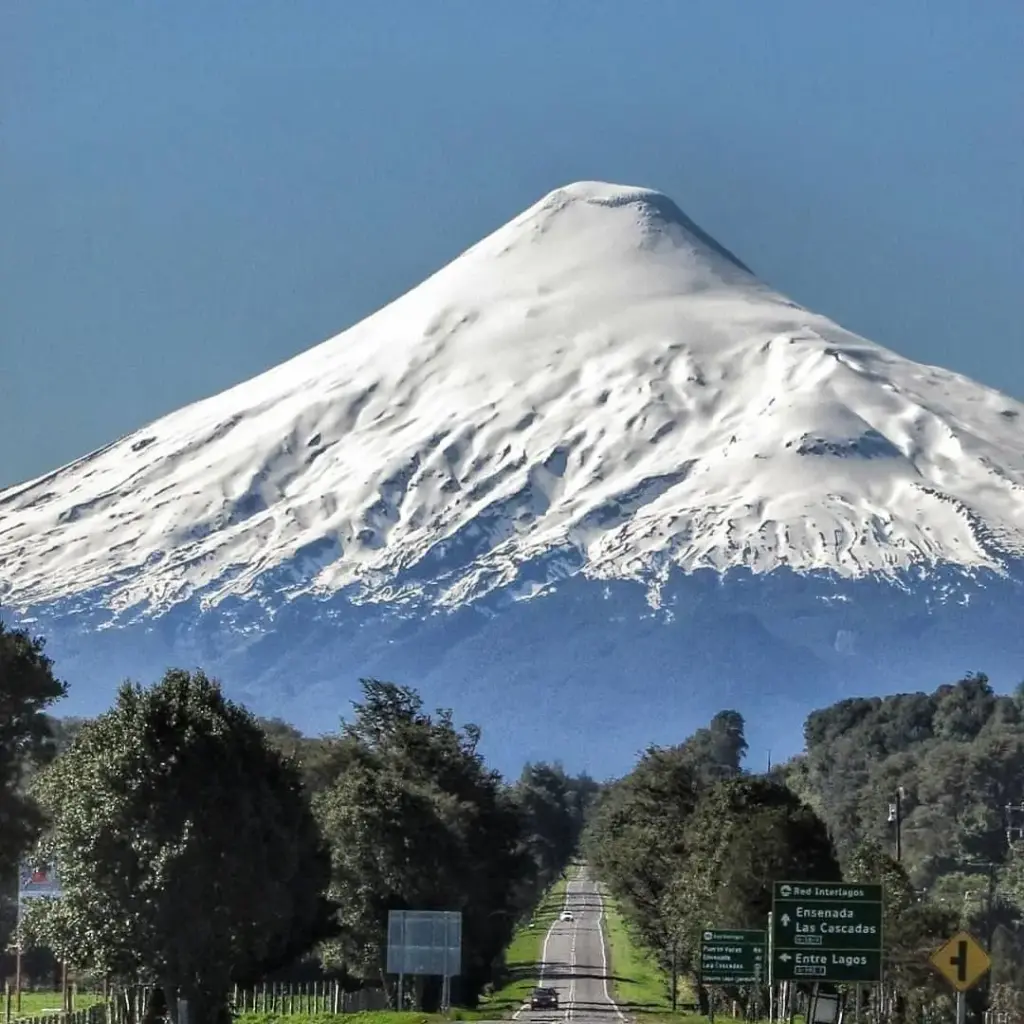 Volcán Osorno nevado al fondo de una carretera rodeada de árboles