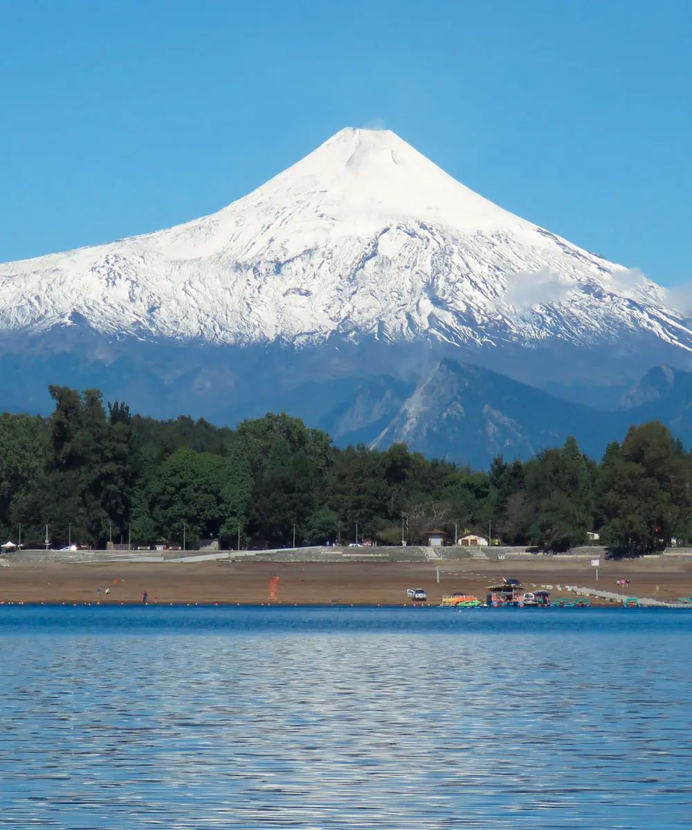 Volcán Villarrica nevado sobre el lago y un bosque en La Araucanía